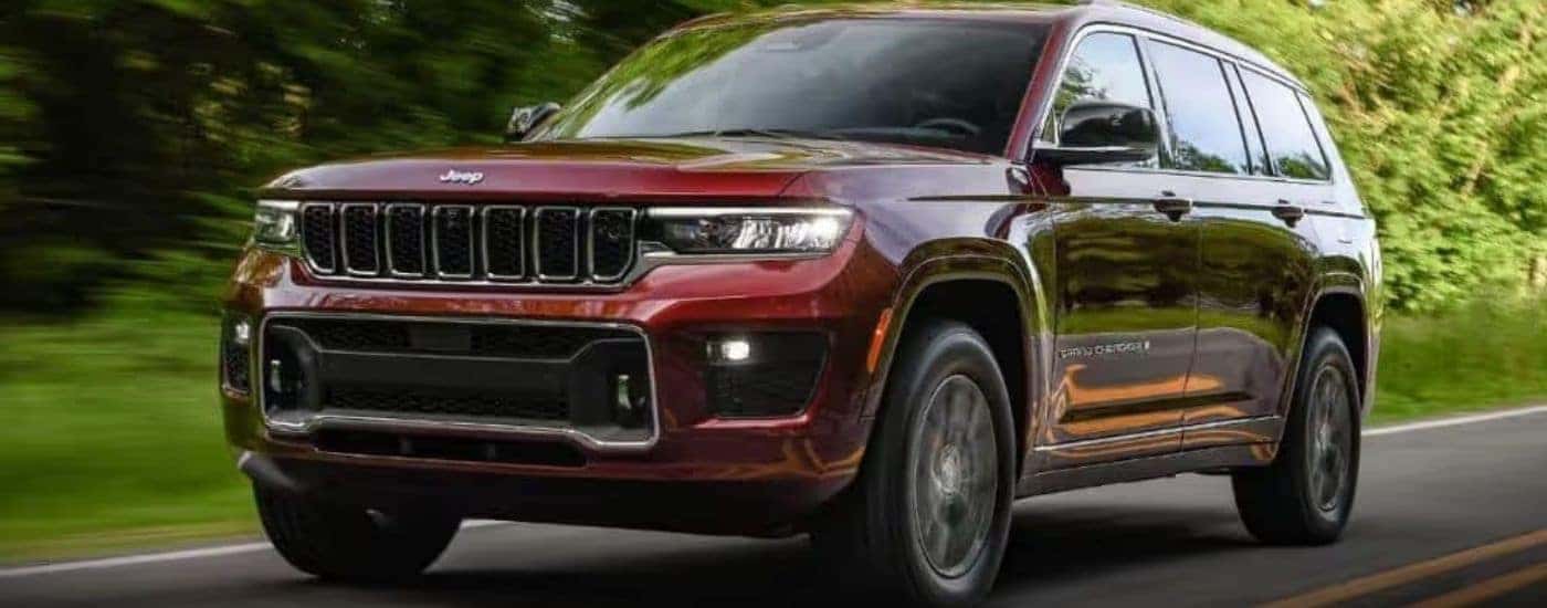 A maroon 2023 Jeep Grand Cherokee is shown driving on a tree-lined road.