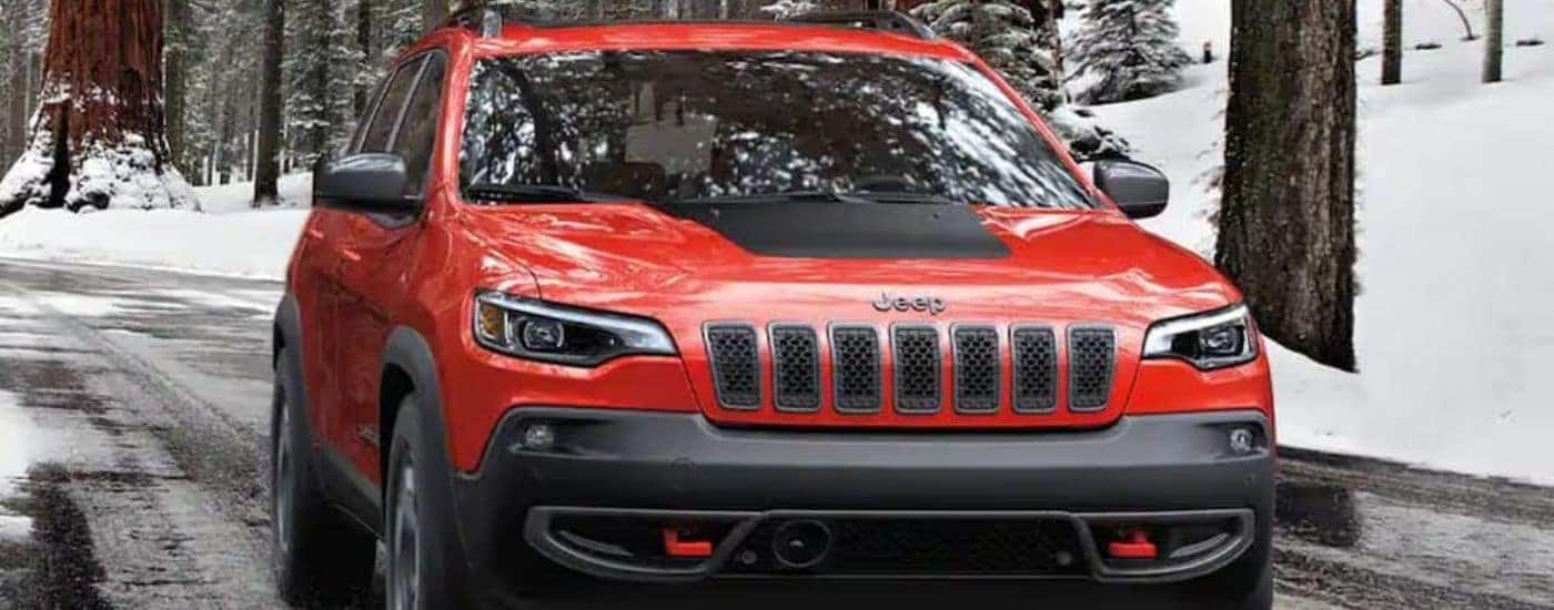 A red 2020 Jeep Cherokee is driving on a snow-lined road.