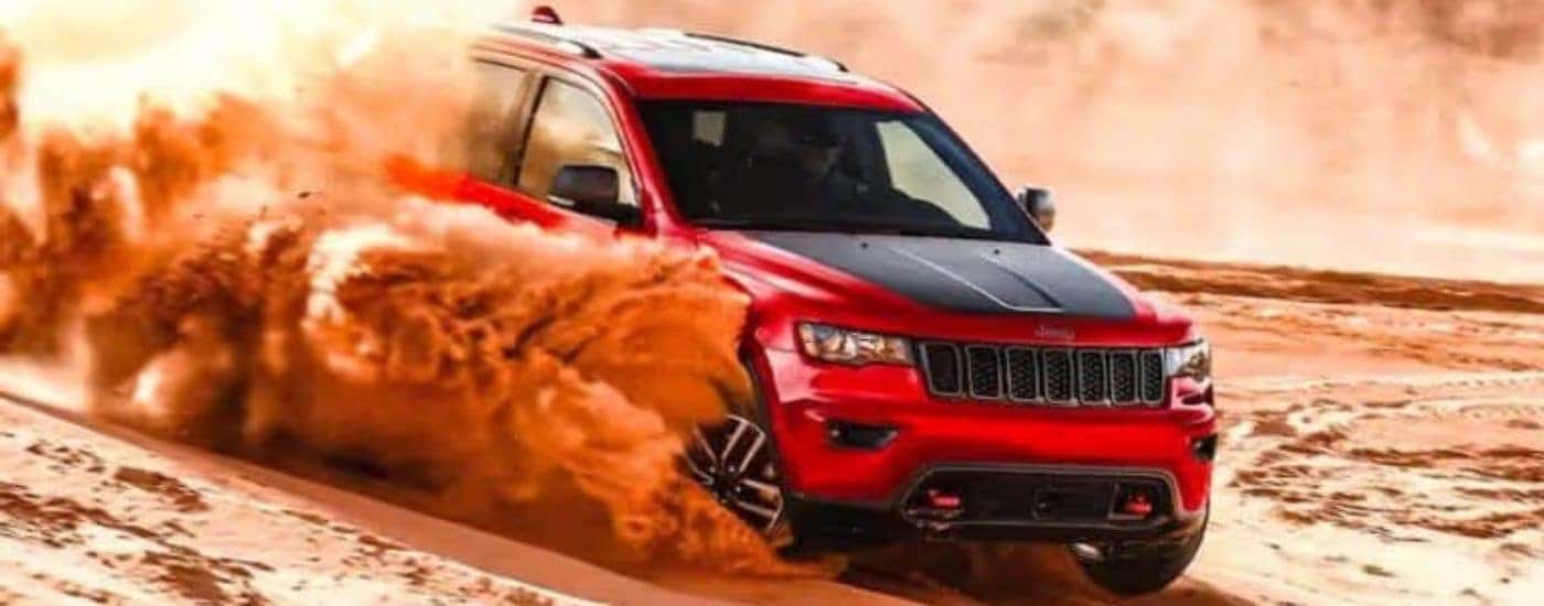 A red 2021 Jeep Grand Cherokee Trailhawk is kicking up sand while driving on a dune.