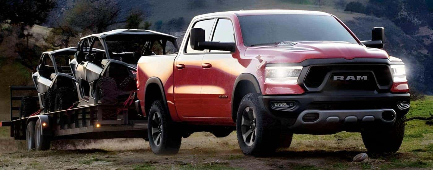 A red 2021 Ram 1500 is towing a trailer with side-by-sides off-road.