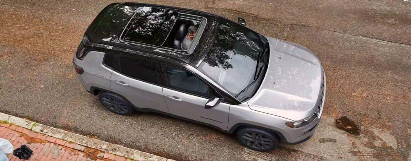A silver 2026 Jeep Compass shown from the top parked next to a curb.