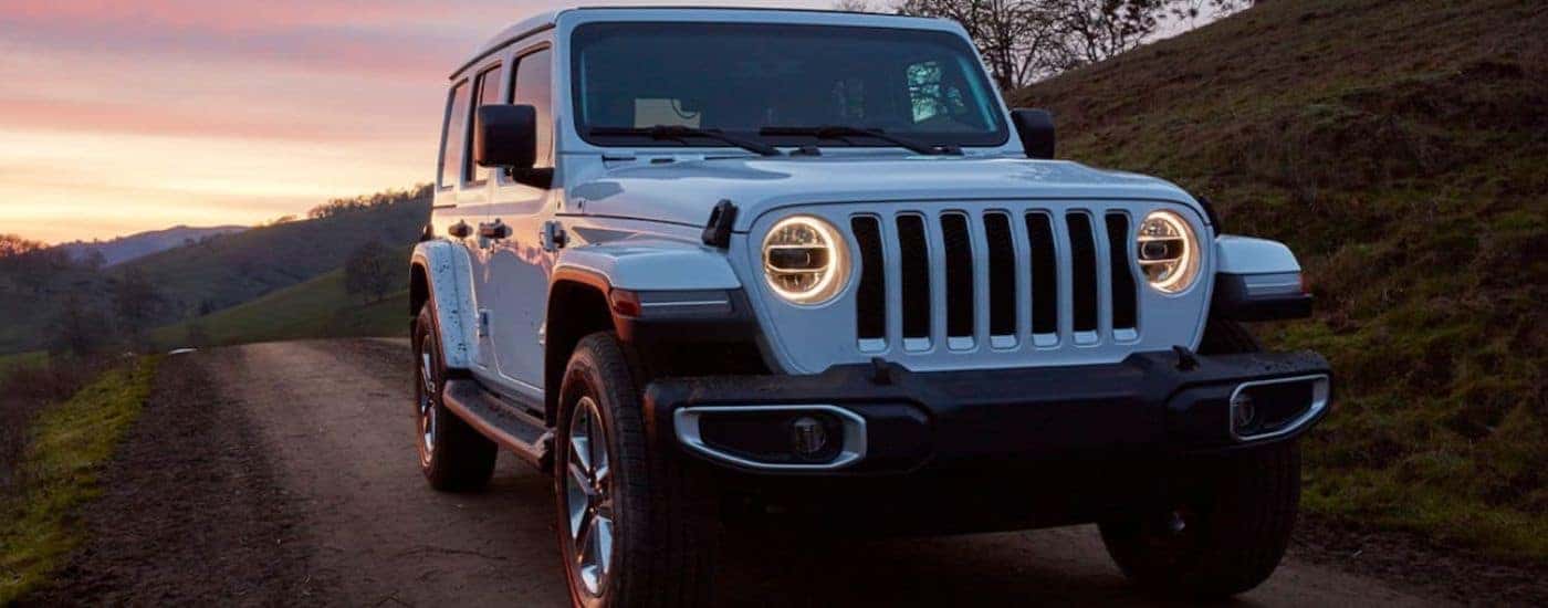 A white 2019 certified pre-owned Jeep Wrangler is shown driving on a road during sunset.