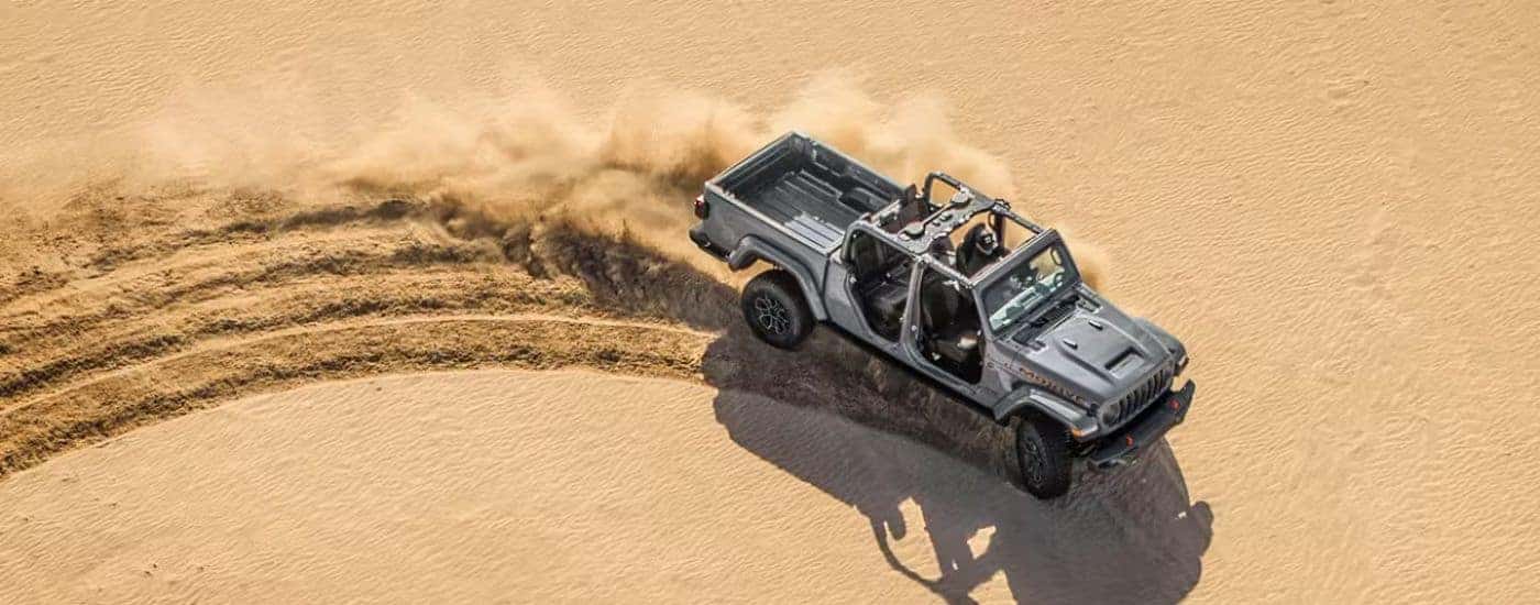 Overhead view of a gray 2026 Jeep Gladiator Mojave X with doors and top removed, driving through sand.