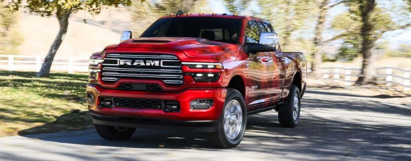 A red 2026 Ram 2500 driving by a white fence.