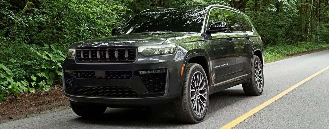Black 2026 Jeep Grand Cherokee driving on a tree-lined road