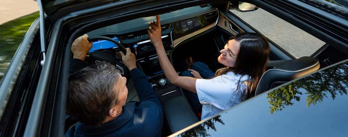 Person opening the moonroof of a silver 2026 Jeep Grand Cherokee