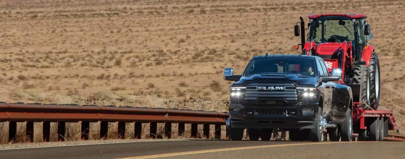 A black 2026 Ram 3500 towing a tractor.