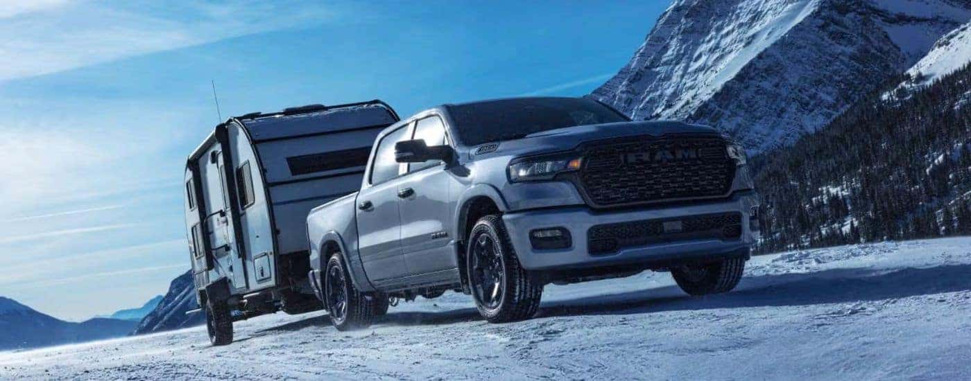 White 2027 Ram 1500 towing a camper in the snow.
