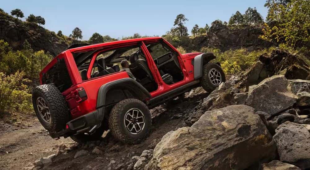 A red 2026 Jeep Wrangler Rubicon without doors driving up rocks.