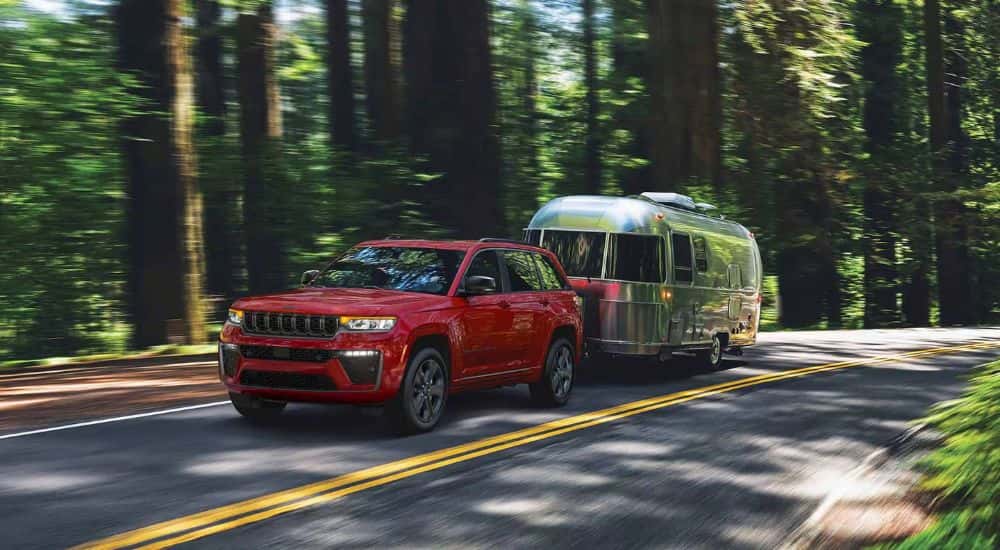 A red 2027 Jeep Grand Cherokee L towing an Airstream by a forest.