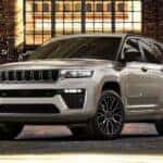A silver 2026 Jeep Grand Cherokee Summit shown parked in front of a brick building.