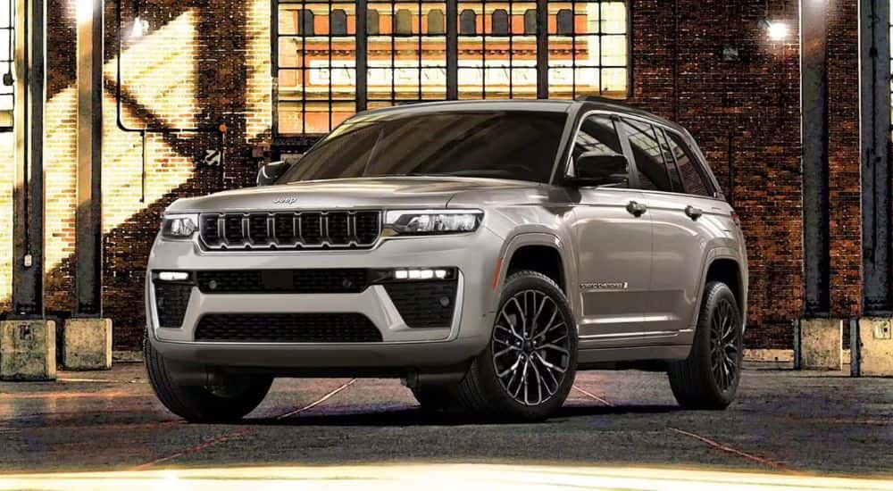 A silver 2026 Jeep Grand Cherokee Summit shown parked in front of a brick building.