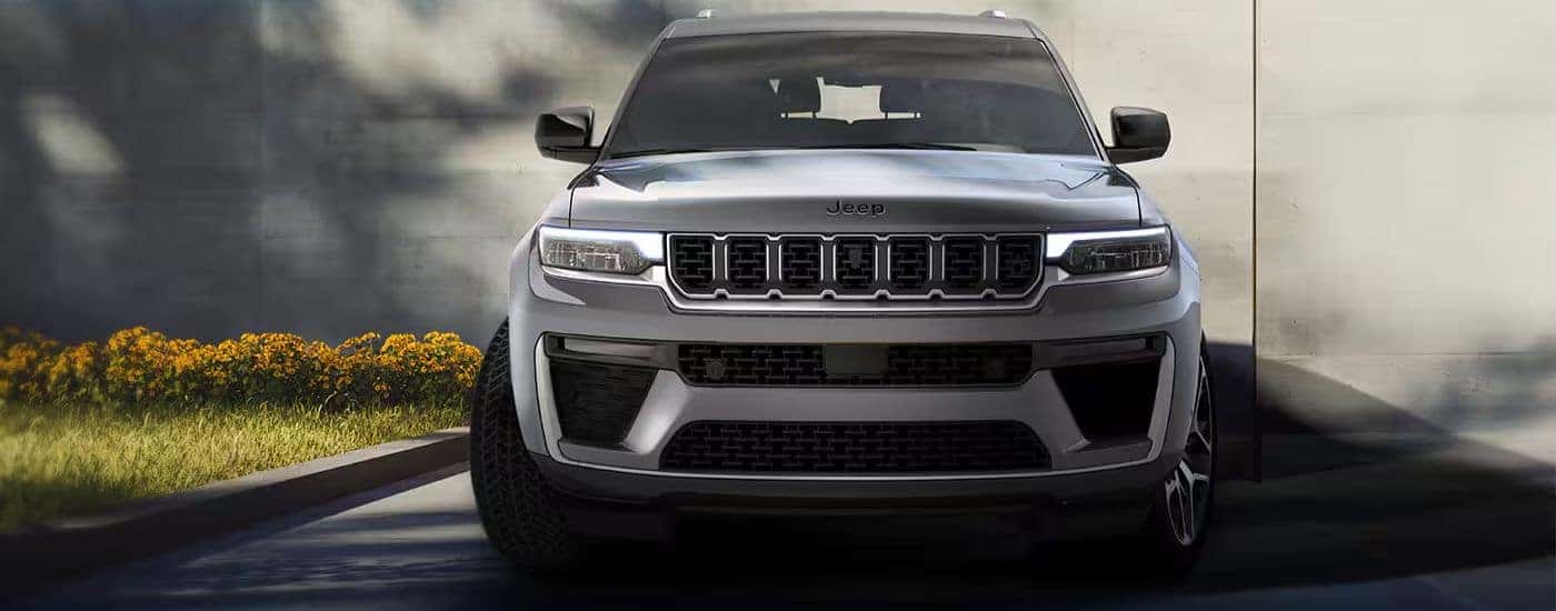 Front grille view of a silver 2026 Jeep Grand Cherokee L parked by flowers.