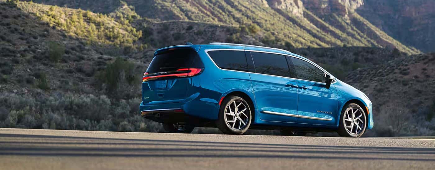 Rear view of a blue 2027 Chrysler Pacifica Pinnacle parked by a mountain.